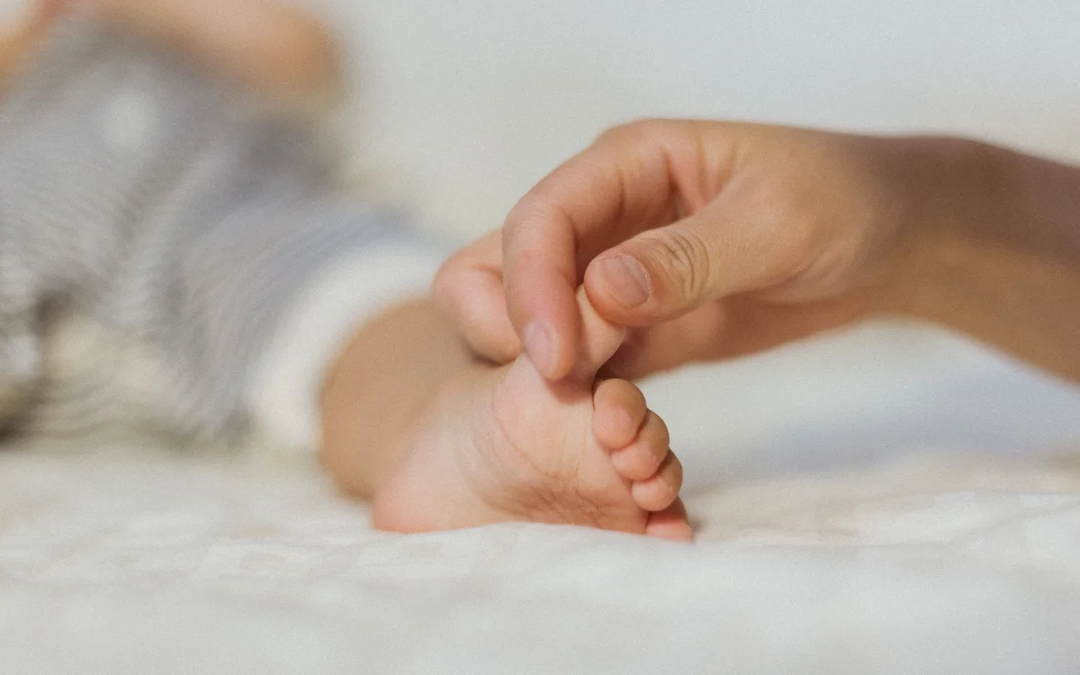 Representative stock photograph of an adult hand gently touching a baby's foot; not a photograph of the child receiving support