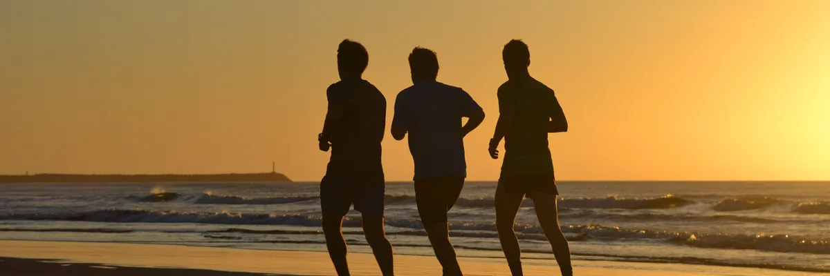 Three men running on a beach at sunset
